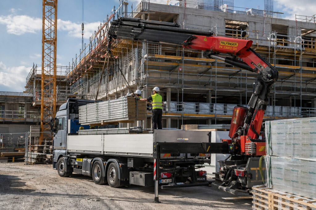 LKW mit Kran entlädt Baumaterial auf Baustelle